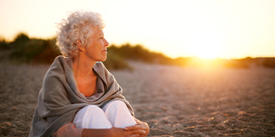 A woman sitting on the beach, relaxed, as the sun rises.