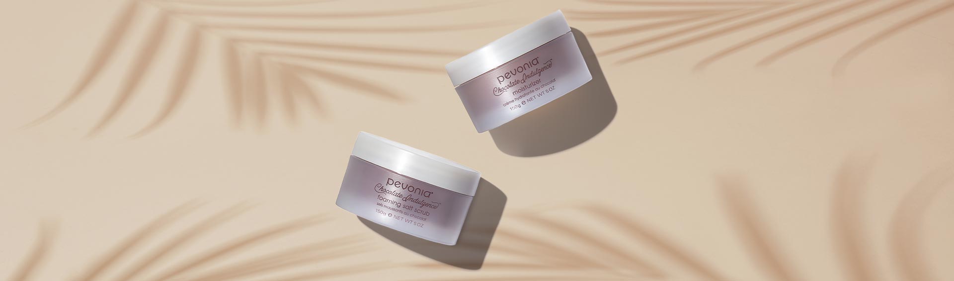 Pevonia Chocolate Indulgence products in a top down shot on a beige background with tropical leaf shadows.