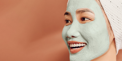A woman with a skincare mask and her hair wrapped up in a towel.
