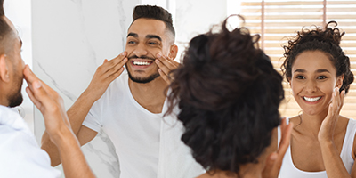 A couple doing their skincare routine in the mirror.
